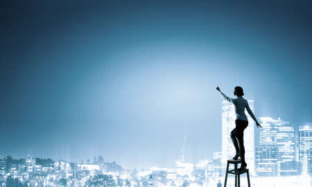 Businesswoman standing on chair and reaching hand to touch somethingの写真素材