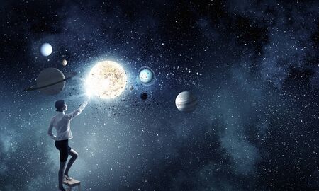 Businesswoman standing on chair and reaching space planetsの写真素材