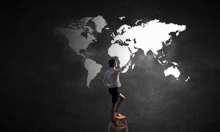 Rear vew of businesswoman climbing chair and touching world map on wallの写真素材