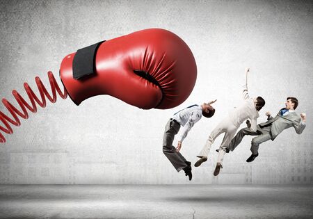 Boxing glove on spring striking group of businesspeople