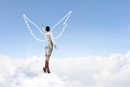 Young businesswoman with drawn wings flying high in skyの写真素材