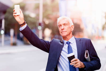 Businessman in suit catching taxi in city with cup of coffee in his handsの写真素材