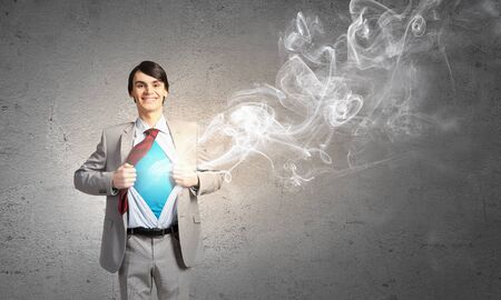 Young smiling businessman acting like super hero and tearing his shirt offの写真素材