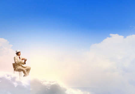 Young businessman in white hat and suit sitting in chairの写真素材
