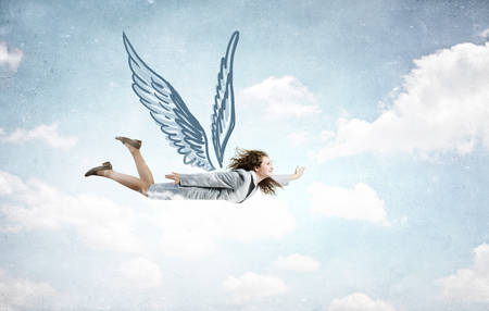 Young businesswoman with drawn wings flying high in skyの写真素材