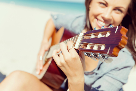 Beautiful young smiling woman playing guitar on beachの写真素材
