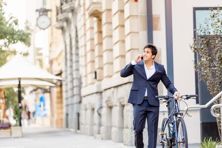 Successful businessman in suit riding bicycle and holding mobile phoneの写真素材