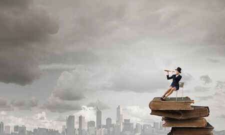 Pretty girl wearing retro hat siting on chair and looking in spyglassの写真素材