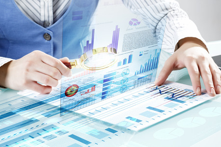 Close up of business person investigating infographs with magnifierの写真素材