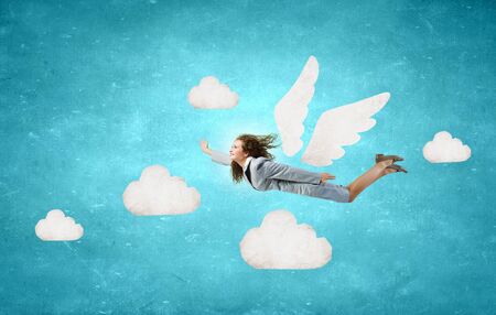 Young businesswoman with drawn wings flying high in skyの写真素材