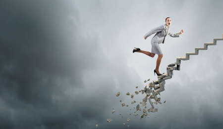 Young businesswoman walking up collapsing staircase representing success conceptの写真素材