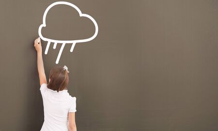 Cute little girl standing with back and drawing on blackboardの写真素材