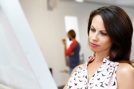 Young caucasian woman standing in an art gallery in front of painting displayed on white wallの写真素材