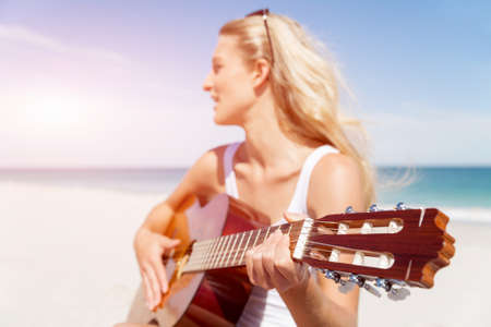 Beautiful young smiling woman playing guitar on beach