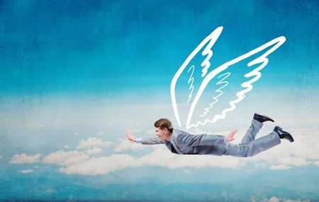 Young businessman with drawn wings flying in skyの写真素材