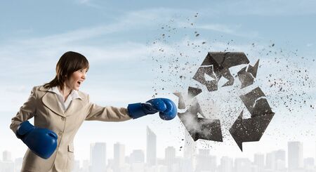 Young businesswoman in blue boxing gloves breaking recycle signの写真素材