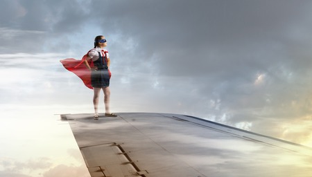 Powerful super hero kid girl standing on wing of flying airplaneの写真素材