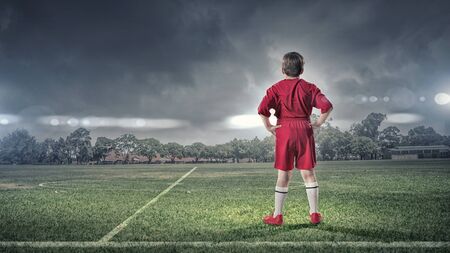 Rear view of kid boy in red uniform on soccer field