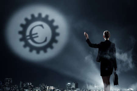 Businesswoman standing with back in darkness and euro sign in spothlightの写真素材