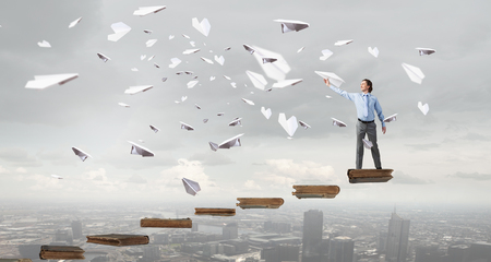 Young businessman in pile of books with paper plane in handの写真素材