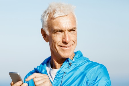 Young male runner with his mobile smart phone standing outdoorsの写真素材