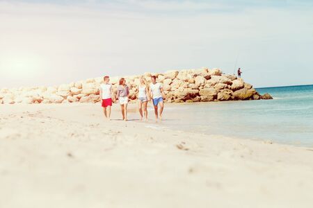Company of young friends on the beach walking along the shoreの写真素材