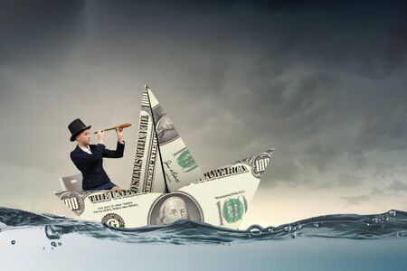 Successful businesswoman sailing on dollar boat in financial seaの写真素材