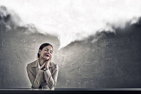 Young businesswoman sitting at table and looking dreamily awayの写真素材