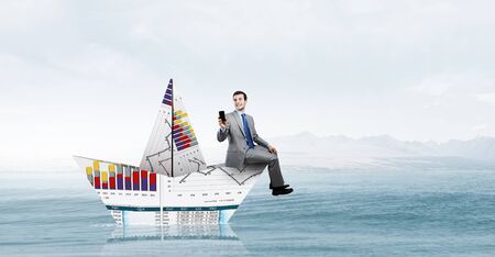 Successful businessman sailing on paper boat in financial seaの写真素材
