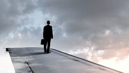 Young businessman standing on edge of airplane wingの写真素材