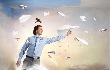 Young businessman in pile of books with paper plane in handの写真素材