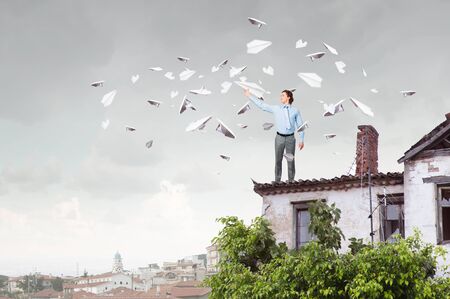 Young businessman in pile of books with paper plane in handの写真素材