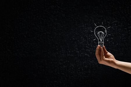 Male hand on dark background showing drawn light bulbの写真素材
