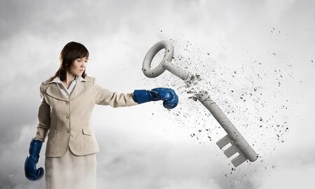 Young businesswoman in blue boxing gloves breaking stone keyの写真素材