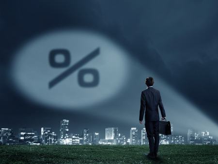 Businessman standing with back and percent sign in spotlightの写真素材