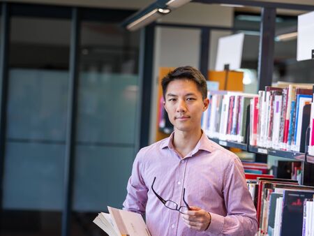 Happy male asian student holding books at the library