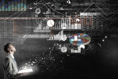 Young businessman with opened book in hands and infographs on backgroundの写真素材