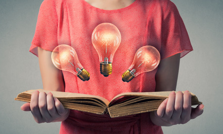 Close view of woman holding book with light bulb on pagesの写真素材