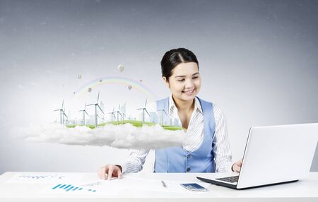 Young smiling businesswoman sitting at table and working with 3d ecology projectの写真素材