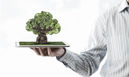Hand of businessman showing tablet with green gears tree on screenの写真素材