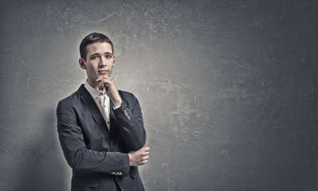 Handsome young man in suit on concrete background looking upの写真素材