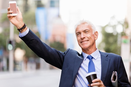 Businessman in suit catching taxi in city with cup of coffee in his handsの写真素材