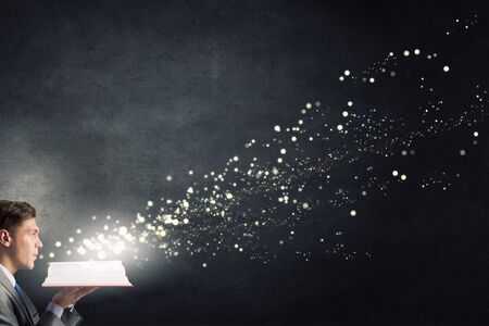 Young businessman with opened book in hands blowing on pagesの写真素材