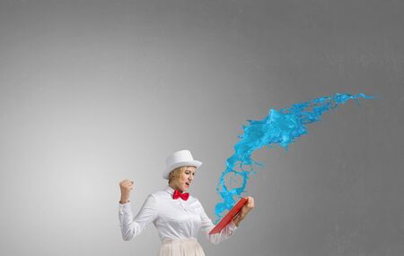 Young woman in white hat with opened book in hands and splashes flying outの写真素材