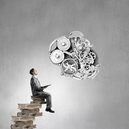 Young businessman sitting on pile with book in handsの写真素材