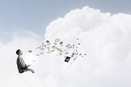 Young businessman sitting on cloud and reading bookの写真素材