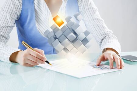 Close up of business person writing with pen and digital cube figure on papersの写真素材