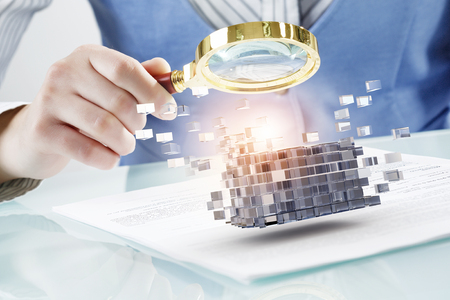 Close up of business person examining digital cube with magnifierの写真素材