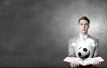 Young businessman with book in hands and soccer ball on pagesの写真素材