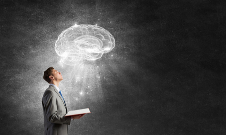 Shocked businessman holding opened book with brain pictureの写真素材